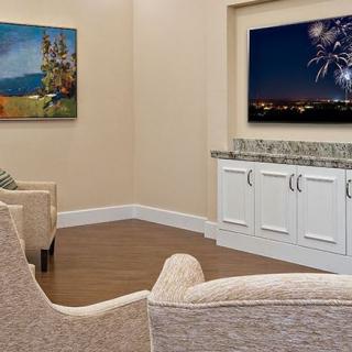 A cozy living room featuring two armchairs, a television displaying fireworks, and colorful artwork on the walls.