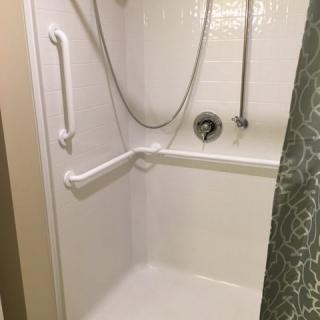 An accessible shower with grab bars and a handheld showerhead, featuring a patterned curtain.