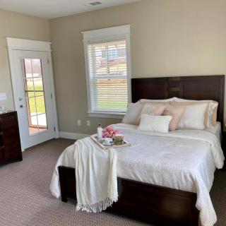 A cozy bedroom featuring a neatly made bed with decorative pillows and a throw blanket, complemented by ample natural light from the windows.