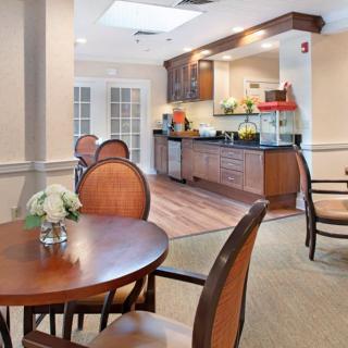 A cozy dining area with round wooden tables and chairs, featuring a kitchenette in the background.
