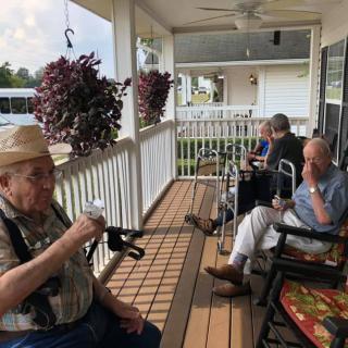 Elderly individuals relaxing on a porch, enjoying drinks and conversation.