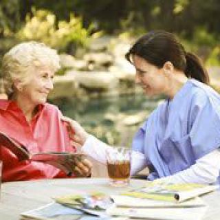 A nurse engaging in conversation with an elderly woman outdoors.