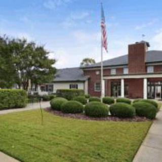 A red-brick building with a well-maintained lawn and an American flagpole in front.