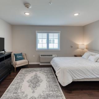 A modern, minimalist bedroom featuring a bed, a television, and a comfortable chair by the window.
