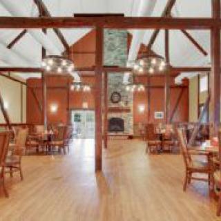 A rustic dining area featuring wooden beams, chandeliers, and a stone fireplace.