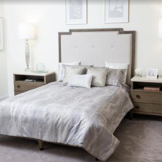 A cozy and elegantly designed bedroom featuring a comfortable bed with soft gray bedding, flanked by wooden nightstands and contemporary lamps.