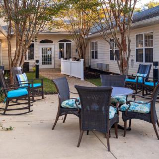 A cozy outdoor patio area with chairs and a table, surrounded by trees and greenery.