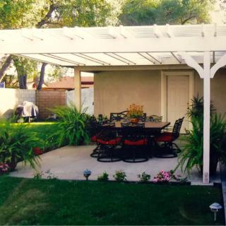 A cozy patio with a pergola, surrounded by lush greenery and garden plants.