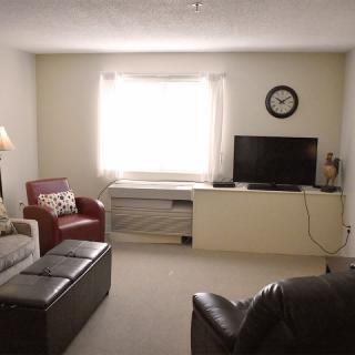 A cozy living room with a sofa, armchair, television, and a clock on the wall.