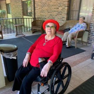 A cheerful elderly woman in a red outfit and hat enjoys her time outdoors in a wheelchair.
