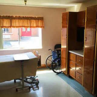 A hospital room with a bed, wheelchair, and wooden furniture.