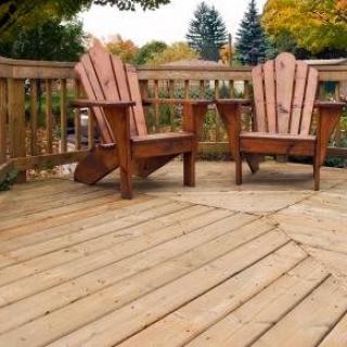 A wooden deck with two Adirondack chairs, surrounded by autumn foliage.