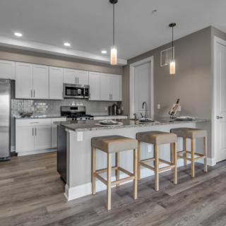A modern kitchen with an island and bar stools, featuring sleek appliances and pendant lighting.