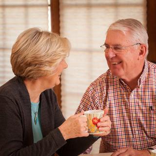 An elderly couple smiling while enjoying a cup of tea indoors.