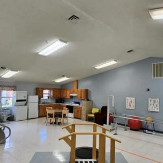 A multi-purpose rehabilitation room with kitchen facilities and therapy equipment.