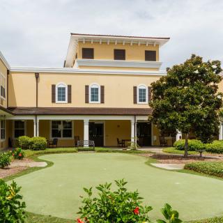 A view of a two-story building with a well-maintained garden and trees in the foreground.