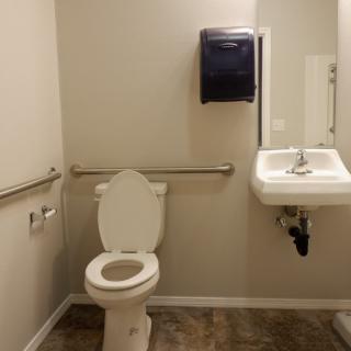 A clean and accessible public restroom featuring a toilet, sink, mirror, and handrails.