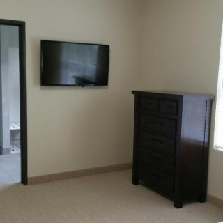 A minimalist bedroom featuring a wall-mounted television and a dark dresser.