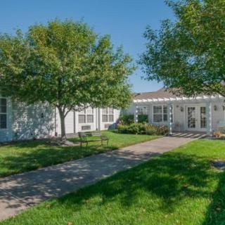 A white residential house with a well-maintained lawn and trees on a sunny day.