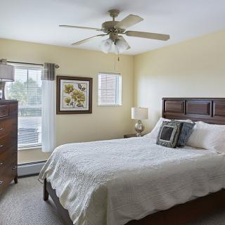 A cozy bedroom with a bed, ceiling fan, and natural light.
