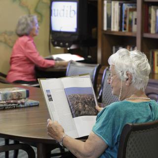 Elderly individuals reading and using a computer in a library.