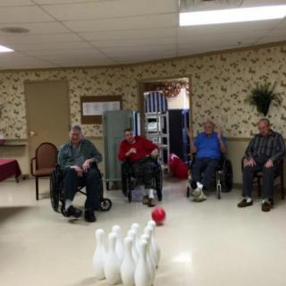 A group of elderly individuals in wheelchairs enjoy a game of indoor bowling at a community center.