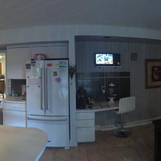 A modern kitchen with a refrigerator, desk, and wall-mounted TV.