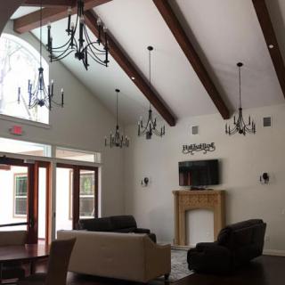 A spacious living room featuring elegant chandeliers and wooden beams, designed to maximize natural light.