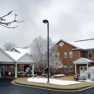 A snowy winter scene featuring a brick building and leafless trees under an overcast sky.
