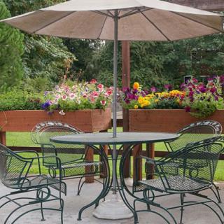 A garden patio set with a table, chairs, and an umbrella surrounded by colorful flower beds.