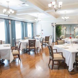An elegant dining room with neatly arranged tables and chairs, featuring chandeliers and large windows with curtains.
