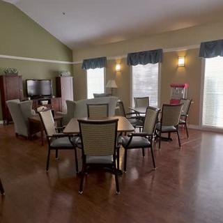 A cozy living and dining area with tables and chairs, featuring large windows and warm lighting.