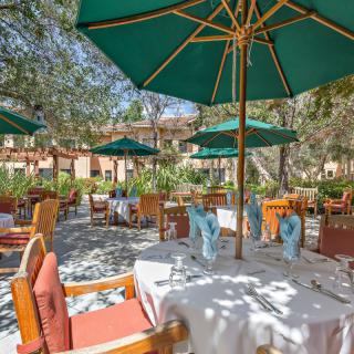 An inviting outdoor restaurant patio with tables set for dining under large green umbrellas.