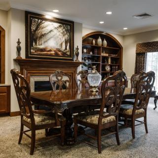 A beautifully furnished dining room with a large wooden table, ornate chairs, a fireplace, and artwork above the mantel.