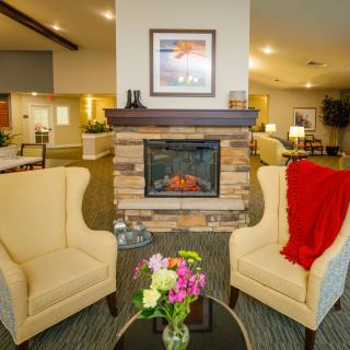 A cozy living room setting featuring a stone fireplace and two armchairs, accented with a vase of fresh flowers.