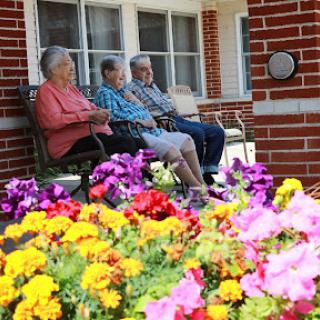 Three elderly individuals enjoy the outdoors on a sunny day, surrounded by vibrant flowers.