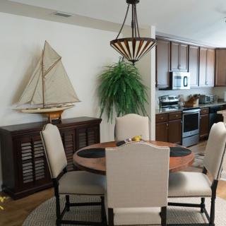 A cozy dining area with a round table and chairs, featuring a sailboat model on the sideboard and connected to a modern kitchen.