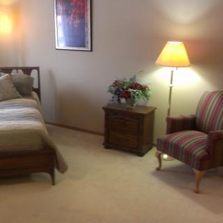 A cozy bedroom with a bed, nightstand, and armchair.
