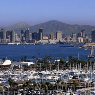 A city skyline with a harbor full of boats and mountains in the background.