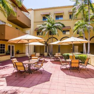 A sunny courtyard with tables and umbrellas surrounded by a yellow building.