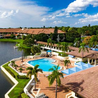 A luxurious tropical resort with a pool and surrounding palm trees by a lake.