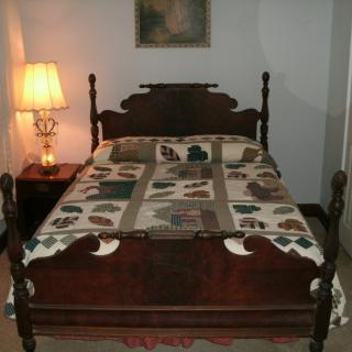 A cozy bedroom featuring a vintage wooden bed frame with a colorful quilt and a bedside lamp.