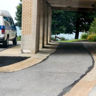 A view of a curved driveway with a parked van and trees in the background.