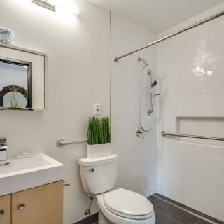 A modern, minimalist bathroom with a sink, toilet, and accessible shower.
