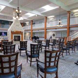 A spacious community lobby with arranged seating, a fireplace, and natural lighting from overhead skylights.