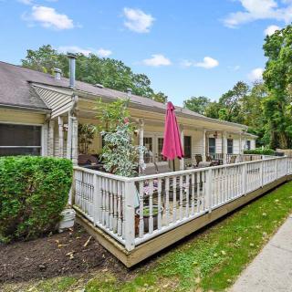 A cozy house with a spacious deck, featuring outdoor seating and an umbrella, surrounded by lush greenery.