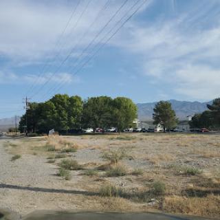A tranquil view of a rural landscape with sparse vegetation, trees, and distant mountains under a clear sky.