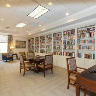 A cozy library with bookshelves, tables, and chairs in a well-lit reading area.