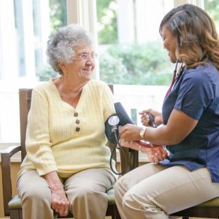 A nurse takes the blood pressure of an elderly woman in a home setting.