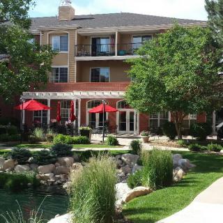 A scenic outdoor view of a building with a landscaped garden and red umbrellas on the patio.